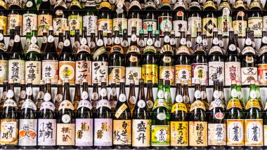 Large collection of Japanese sake bottles with multiple colored labels arranged on shelfs taken at temple in Tokyo.