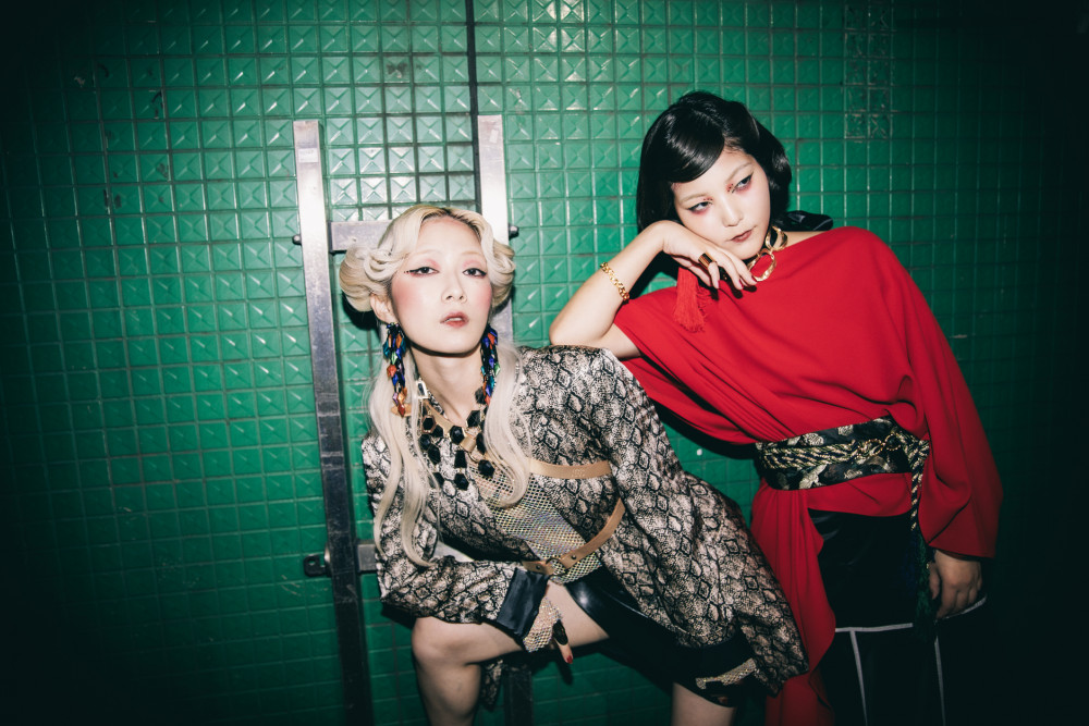 two women, one in a design suit jacket and one in a red fabric dress with a black-and-white fabric belt