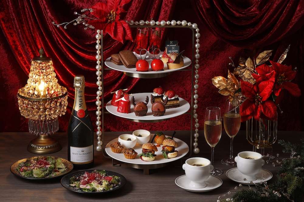 Dark chocolate and strawberry-flavored desserts sit on tiered trays with poinsettia flowers for The Strings Omotesando Christmas-themed Afternoon Tea spread.
