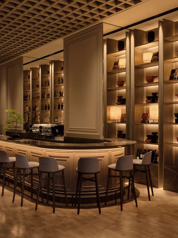 Janu Bar in Tokyo, with warm ambient lighting and the counter with bonsai. 6 chairs placed in front of the marble counter.