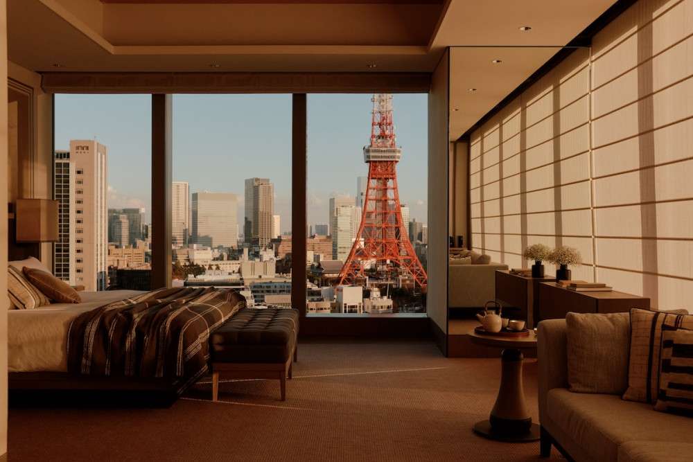 The photo of the bed room at Janu Tokyo, the golden hour and light is hitting the room through large window where you can see the bottom of the Tokyo Tower.