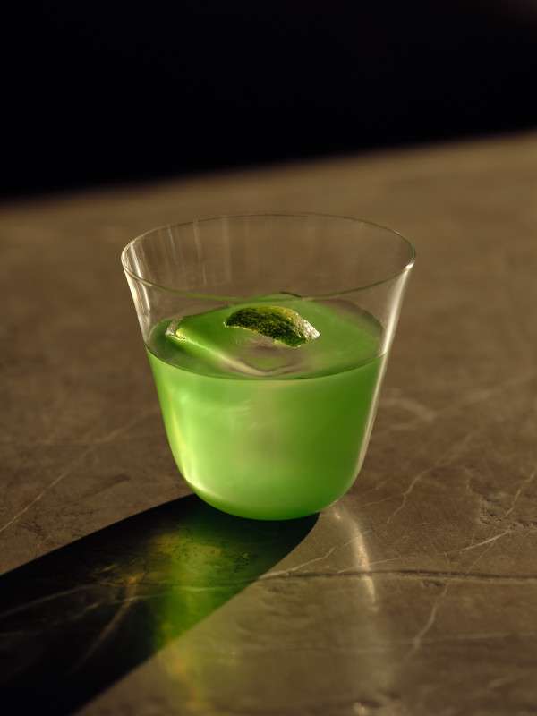 A close-up photo of Janu Bar's limited cocktail, green negroni, featuring Japanese citrus and pine-flavored gin. The drink is vibrant green like Japanese green tea.