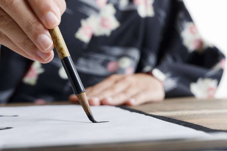 A person wearing a kimono makes the first brushstroke in a Japanese calligraphy workshop using a traditional calligraphy brush.