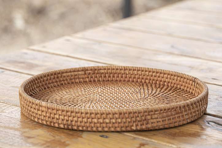 A short bamboo basket sits on a wooden table outdoors, showcasing traditional Japanese takezaiku basketry.
