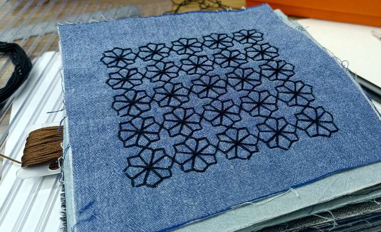 Close-up of white sashiko embroidery stitched into a floral pattern on indigo fabric, showcasing the traditional Japanese stitching technique.