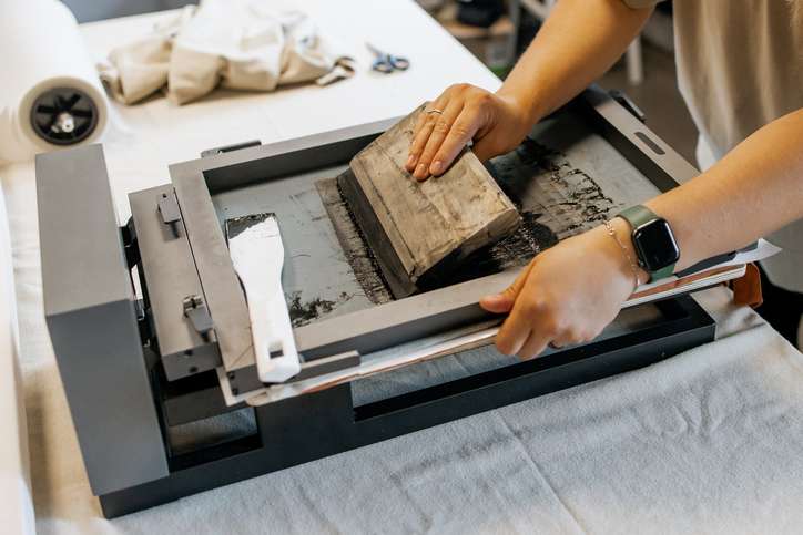 Manual Silk Screen Printing on Fabric – Close-up of Hands Working with Screen Printing Machine in Workshop