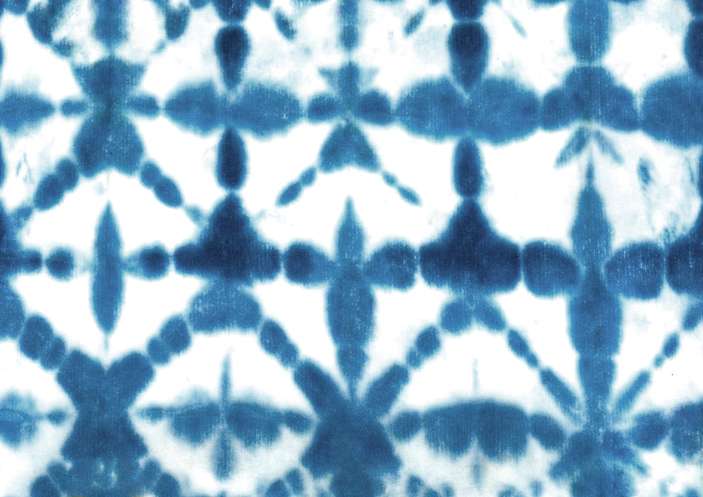 Blue indigo-dyed cotton cloth with repeating white diamond patterns folded on a wooden table.